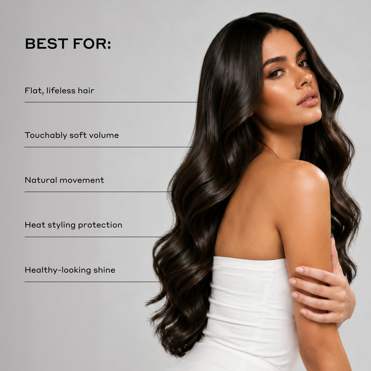 A woman with long, dark, wavy hair wearing a white strapless top, shown against a light gray background with text listing benefits such as flat, lifeless hair, touchably soft volume, natural movement, heat styling protection, and healthy-looking shine.